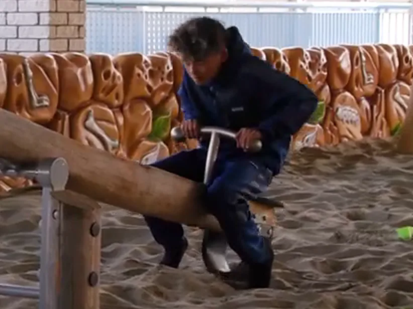 Een kind op een wip in de overdekte zandbak van Spelen bij Beelen, met de rotswand op de achtergrond